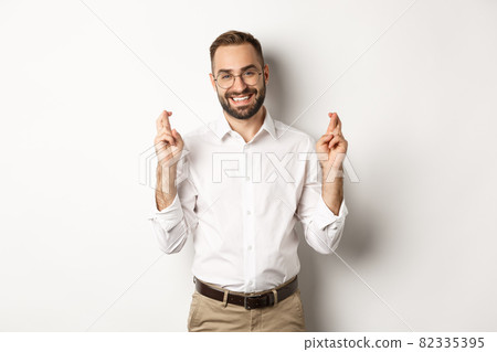 Hopeful optimistic man making a wish, cross fingers and praying, standing over white background Hopeful optimistic man making a wish, cross fingers and praying, standing over white background 82335395