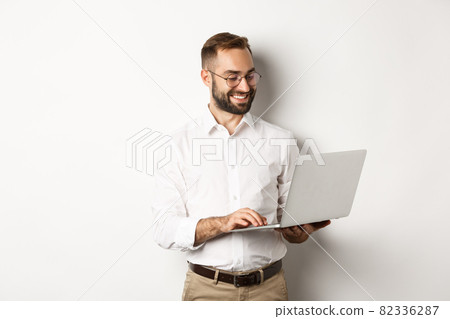 Business. Handsome businessman working on laptop, answering messages and smiling, standing over white background 82336287