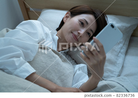 Middle woman using a smartphone in bed 82336736