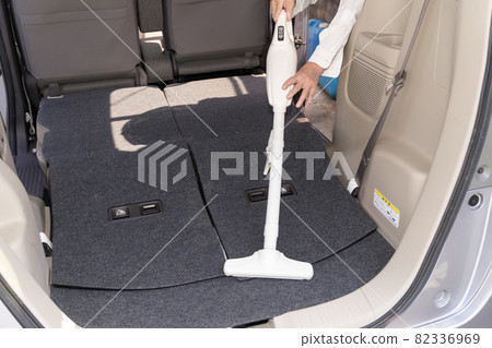 Senior man cleaning the luggage compartment of a car with a handy vacuum cleaner 82336969