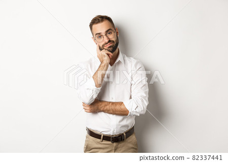 Unamused bearded man in glasses looking displeased at camera, standing moody over white background 82337441