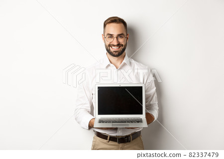 Handsome businessman in glasses, showing laptop screen and smiling happy, standing over white background Handsome businessman in glasses, showing laptop screen and smiling happy, standing over white background 82337479