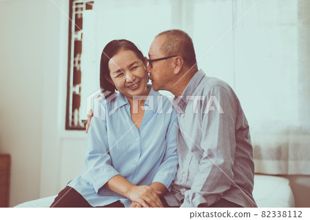 Happy couple senior asian kiss to cheek togeter on bed at home Happy couple senior asian kiss to cheek togeter on bed at home 82338112