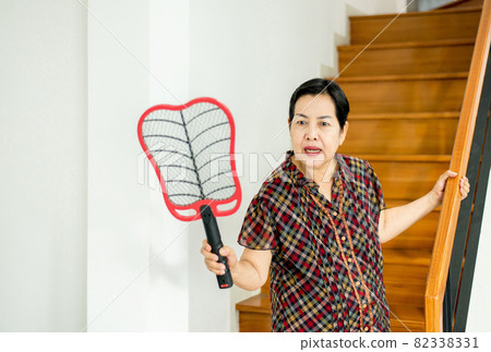 Elderly woman using mosquito swatter at home,Female with mosquito electric net racket 82338331