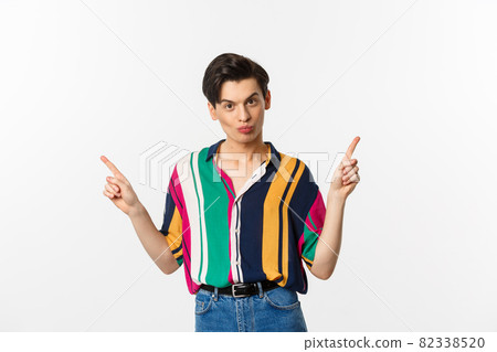 Handsome gay man pointing fingers sideways, showing two variants, demonstrate promos, standing over white background 82338520