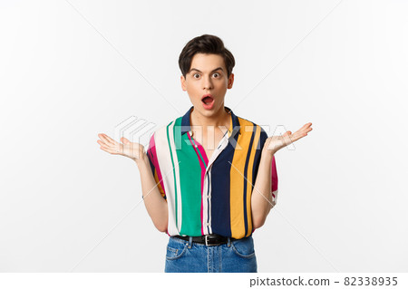 Image of surprised young male model staring at camera, spread hands sideways in complete disbelief, standing over white background 82338935