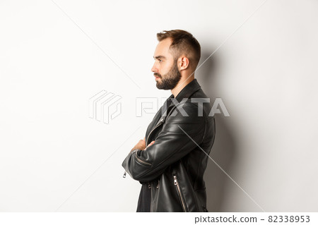Profile of handsome serious man in leather jacket, looking left, holding hands on chest confident, white background 82338953