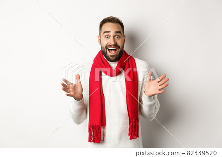Christmas holidays and celebration concept. Bearded guy looking surprised at new year promo offers, gasping amazed, wearing red scarf and sweater, white background Christmas holidays and celebration concept. Bearded guy looking surprised at new year promo offers, gasping amazed, wearing red scarf and sweater, white background 82339520