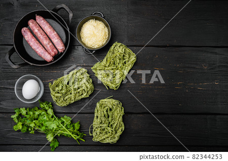 Fresh green pasta and sausages, on black wooden table background, top view flat lay, with copy space for text 82344253