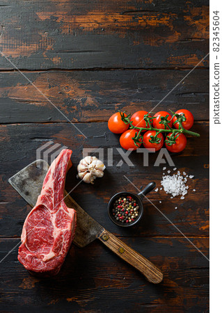 Raw tomahawk steak on meat cleaver. Organic farm marbled prime black angus beef. Dark wooden background. top view. With seasonings, peppercorns, rosemary,salt,garlic. space for text 82345604