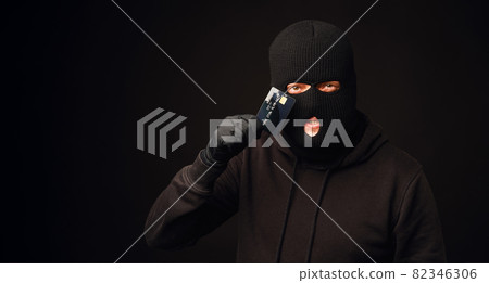 Thief in black balaclava holding black credit card. Banking and non cash thief concept Thief in black balaclava holding black credit card. Banking and non cash thief concept 82346306