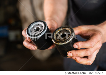 An auto mechanic holds a new and used oil filter. 82346514