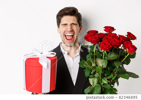 Image of sad guy in suit, got rejected and crying, holding bouquet of roses and present, standing miserable against white background Image of sad guy in suit, got rejected and crying, holding bouquet of roses and present, standing miserable against white background 82346895