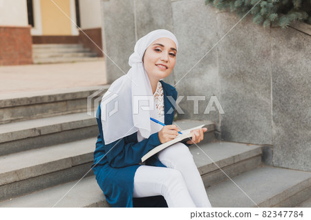 Female middle eastern college student sits on stairs in university campus. Education and knowledge concept. Female middle eastern college student sits on stairs in university campus. Education and knowledge concept. 82347784