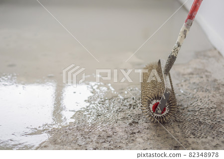 plasterer during floor covering works with self-levelling cement mortar, uses a needle roller plasterer during floor covering works with self-levelling cement mortar, uses a needle roller 82348978