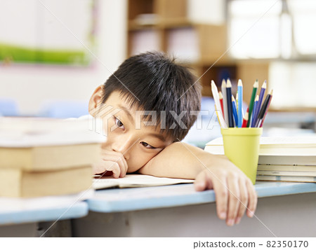 asian elementary schoolboy looking tired and exhausted resting his head on desk in classroom asian elementary schoolboy looking tired and exhausted resting his head on desk in classroom 82350170