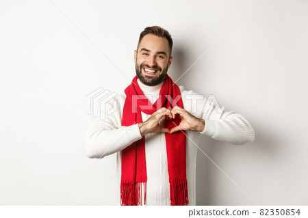 Christmas holidays and New Year concept. Happy father showing heart sign and smiling, I love you gesture, wearing winter sweater and scarf, white background 82350854