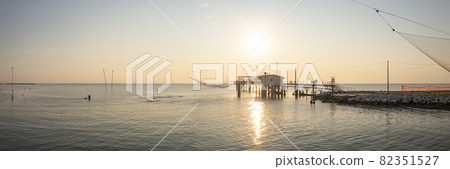 Landscape of fishing huts at sunrise with typical italian fishing machine, called ""trabucco"",Lido di Dante, fiumi uniti Ravenna near Comacchio valley. Landscape of fishing huts at sunrise with typical italian fishing machine, called ""trabucco"",Lido di Dante, fiumi uniti Ravenna near Comacchio valley. 82351527