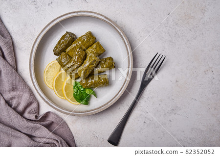 Dolma, stuffed grape leaves with rice and meat in light plate with black fork and linen napkin Dolma, stuffed grape leaves with rice and meat in light plate with black fork and linen napkin 82352052