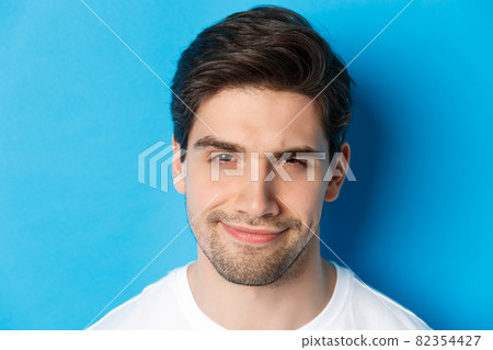 Headshot of thoughtful handsome man, looking intrigued and squinting, thinking about something, standing over blue background Headshot of thoughtful handsome man, looking intrigued and squinting, thinking about something, standing over blue background 82354427