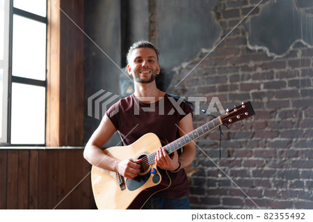 Man with acoustic guitar against brick wall playing music singing songs enjoy life Medium shoot 82355492