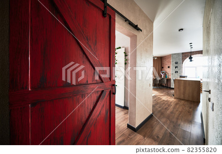 View of big red door to the corridor leading to the kitchen. Interior of appartment in loft style with wooden flooring. Concept of flat decor. 82355820