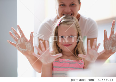 Mom and little girl showing palms of hands in flour Mom and little girl showing palms of hands in flour 82355943