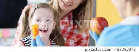 Doctor holding jar of capsules and red apple in front of child and mother in clinic Doctor holding jar of capsules and red apple in front of child and mother in clinic 82356078
