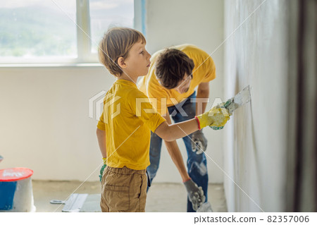 Man with his son makes repairs at home, he teaches children to plaster the walls with a spatula in his hands 82357006