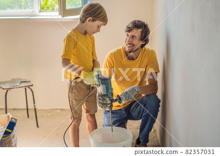 Man with his son makes repairs at home, he teaches children to plaster the walls with a spatula in his hands Man with his son makes repairs at home, he teaches children to plaster the walls with a spatula in his hands 82357031