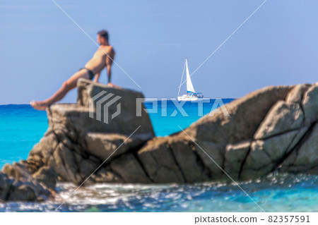 Man sunbathing on a rock against sailboats in Vibo Valentia, Calabria, Southern Italy 82357591