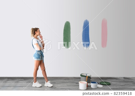 Beautiful woman is standing front of the wall and try to decide the color of painting wall. Beautiful woman is standing front of the wall and try to decide the color of painting wall. 82359418