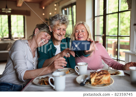 Happy senior friends having coffee and cake and taking selfie indoors at home. 82359745