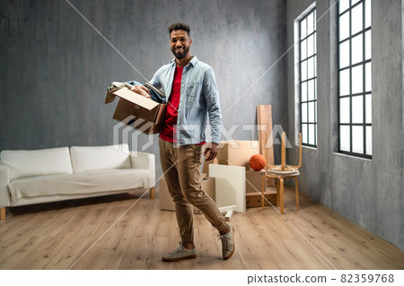 Happy young man holding packing boxes moving home, looking at camera, new living concept. 82359768