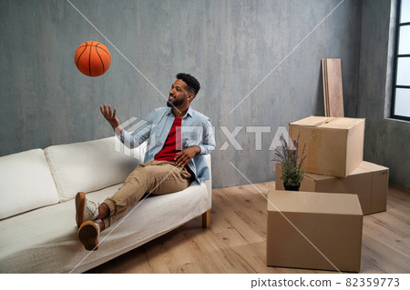 Happy young man with basketball celebrating moving home surrounded by packing boxes, new living concept. 82359773