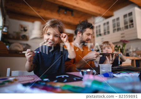 Mature father with two small children resting indoors at home, painting pictures. Mature father with two small children resting indoors at home, painting pictures. 82359891