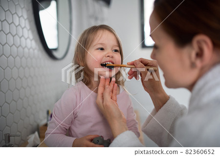 Mother with small daughter brushing teeth indoors in bathroom in the evening or morning. Mother with small daughter brushing teeth indoors in bathroom in the evening or morning. 82360652