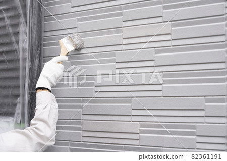 Hands of a painter who paints the exterior walls of a detached house with a brush 82361191