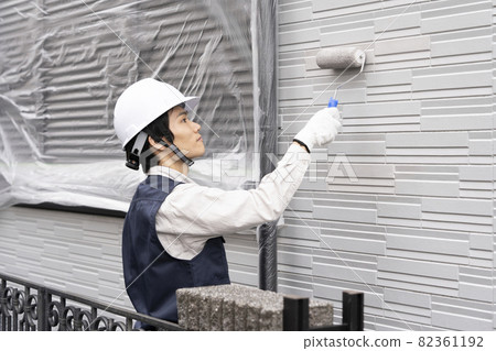 A painter who paints the exterior walls of a detached house with a roller 82361192