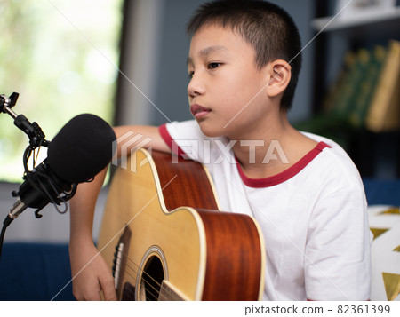 asian boy with microphone recording song and playing guitar in living room. 82361399