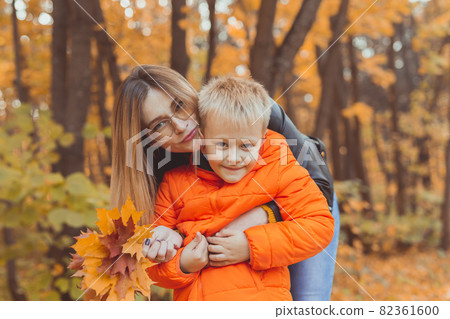 Mother hugging her child during walk in autumn park. Fall season and single parent concept. Mother hugging her child during walk in autumn park. Fall season and single parent concept. 82361600