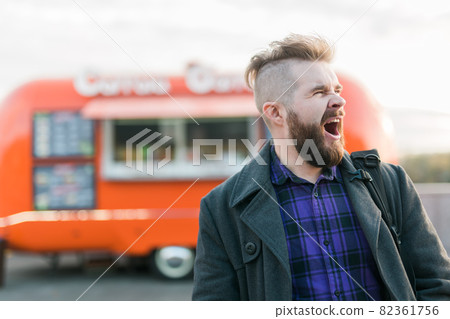 Bearded man in the street yawns with opened mouth stands at a food truck background. Sleepy people and lazy concept. 82361756