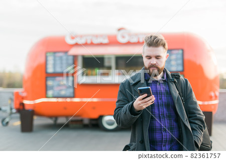 Portrait of handsome young man with smartphone standing in front of food truck Portrait of handsome young man with smartphone standing in front of food truck 82361757