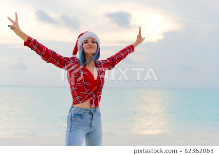 Happy young woman in Santa hat on the beach near the sea. Travel Concept Happy young woman in Santa hat on the beach near the sea. Travel Concept 82362063