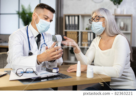 Doctor using modern thermometer for examining aged woman Doctor using modern thermometer for examining aged woman 82363221