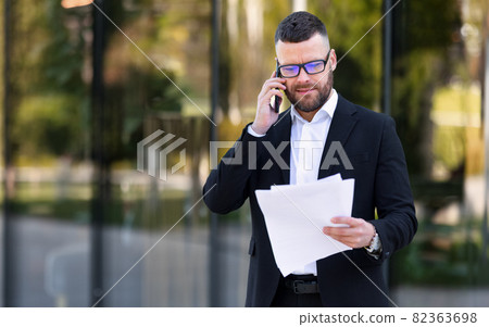 Focused serious businessman lawyer talking by mobile phone with client and reading contract paper 82363698