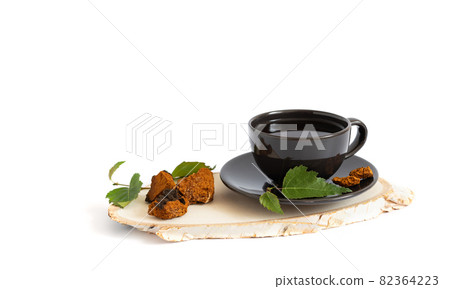 Chaga tea. Chaga infusion in a black cup on a wooden board isolated on a white background. Drink with birch mushroom. 82364223