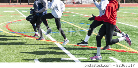High school girls track team doing sprint form drills on a turf field in winter 82365117