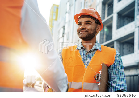 Two men engineers in workwear shaking hands against construction site. 82365610