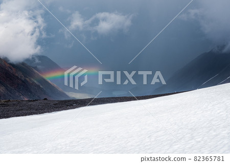 Rainbow over a winter snow mountain valley. Atmospheric alpine landscape with snowy mountains with rainbow in rainy and sunny weather. Rainbow over a winter snow mountain valley. Atmospheric alpine landscape with snowy mountains with rainbow in rainy and sunny weather. 82365781